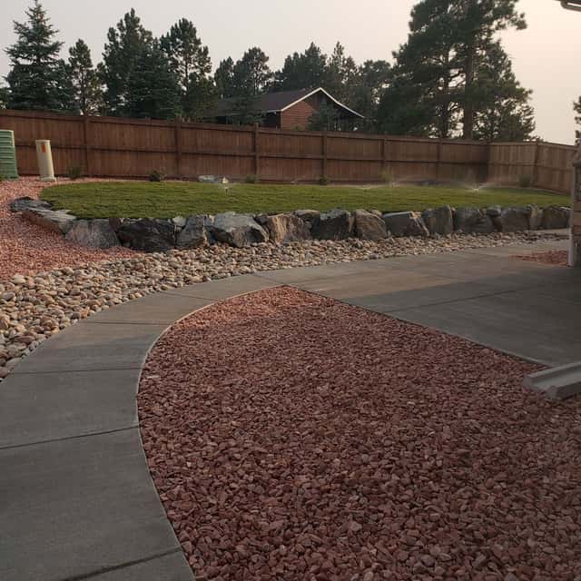 Concrete walkway edged with red rock and boulders along a fence — Angel's Landscaping LLC, Castle Rock, CO