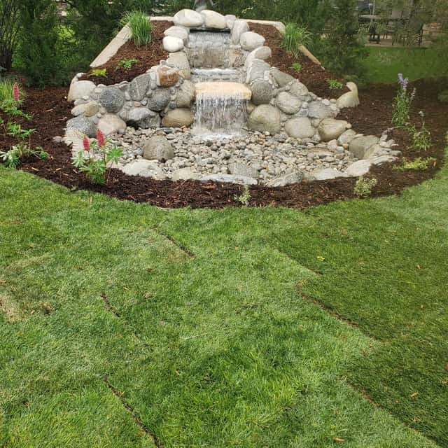 Boulder waterfall feature set in mulch beside a new sod lawn — Angel's Landscaping LLC, Castle Rock, CO